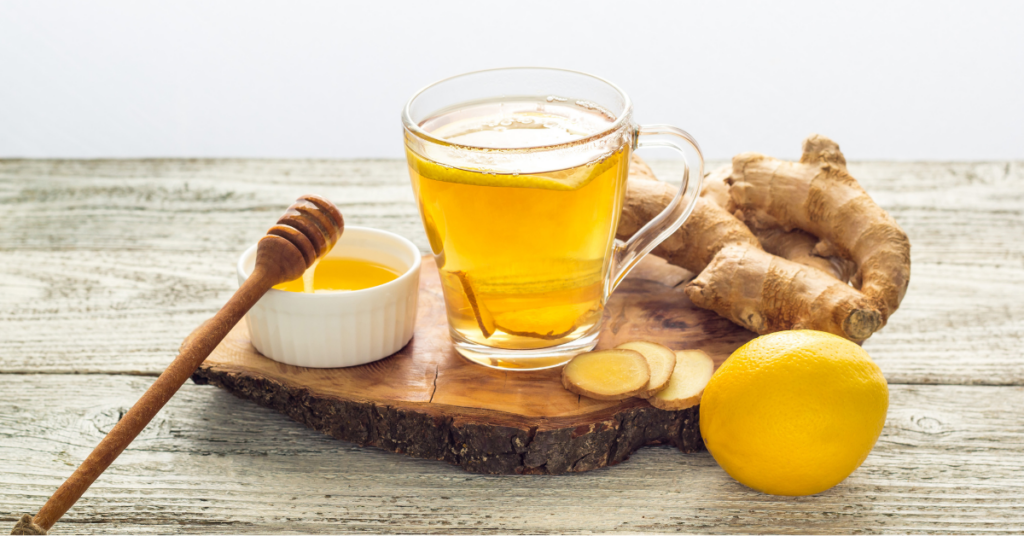 A glass of freshly brewed ginger tea with lemon, honey, and sliced ginger on a rustic wooden board, highlighting a popular common home remedy for digestion and colds.