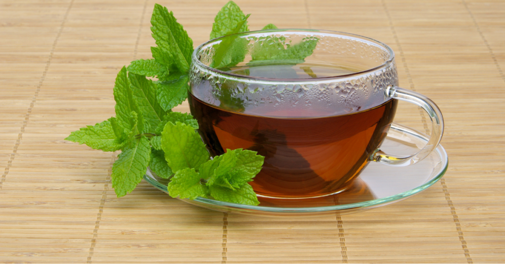 A clear glass cup of freshly brewed peppermint tea, surrounded by vibrant mint leaves, emphasizing a soothing common home remedy for headaches and digestion.