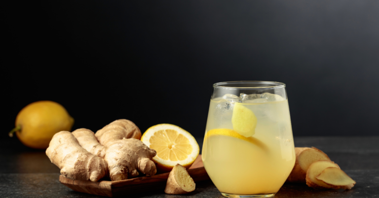 A refreshing glass of ginger lemonade sits on a dark surface, garnished with lemon slices and a piece of ginger. Surrounding the glass are fresh ginger roots, lemon wedges, and sliced ginger, symbolizing the natural ingredients used for creating ginger paste and beverages.